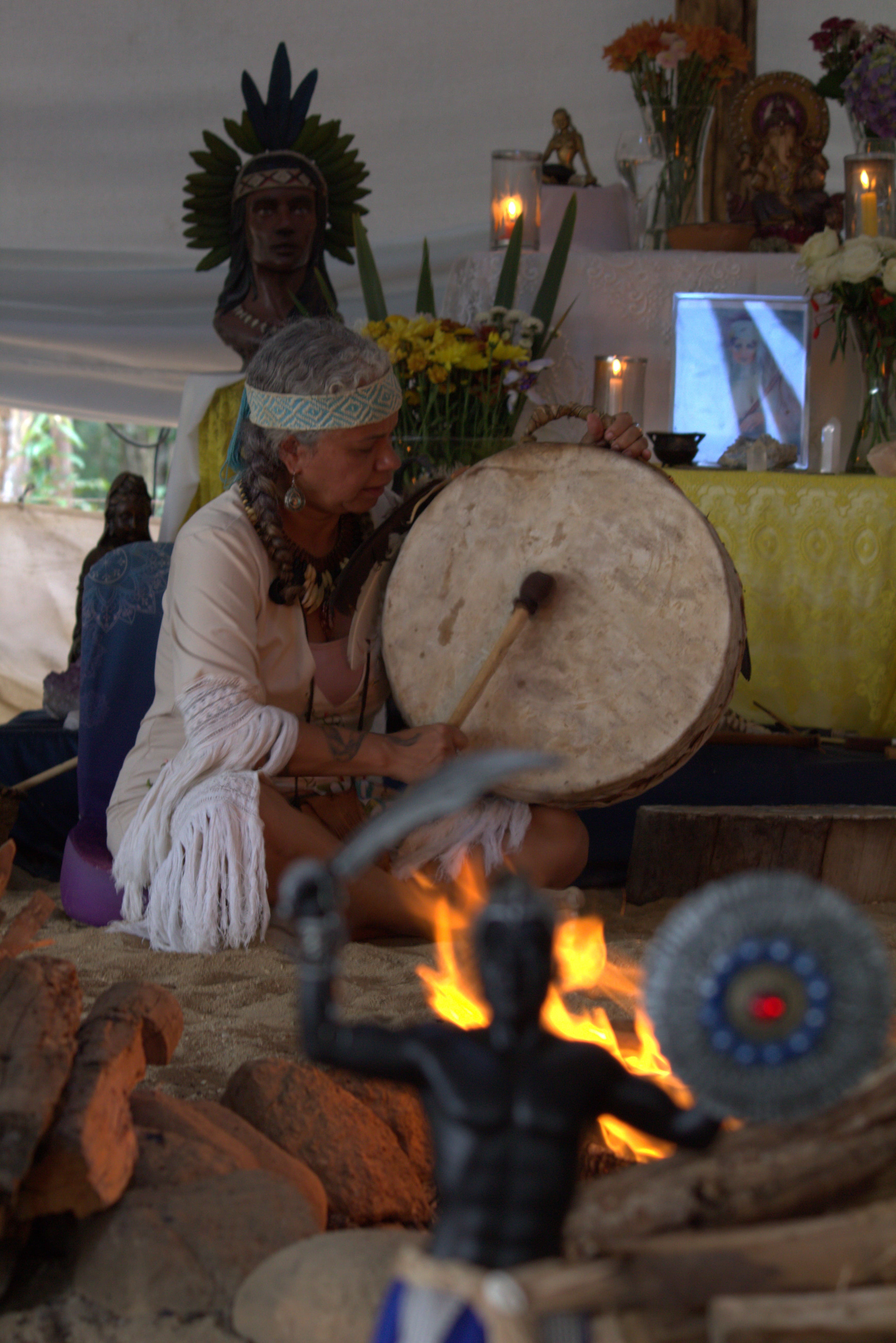 Xamã Ayala com cocar e tambor diante do altar ritualístico das Terras de Anahí